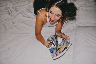 微笑的女人躺在床上,阅读杂志
